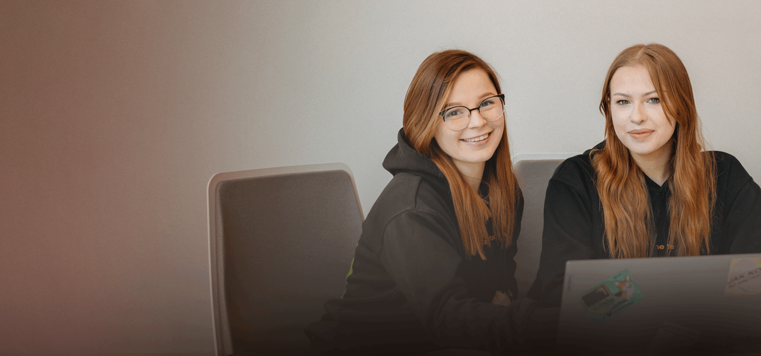 dwie uśmiechnięte kobiety siedzą przy biurku